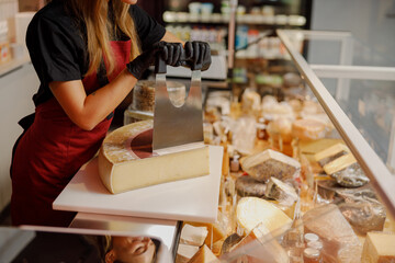 In a gourmet shop filled with exquisite cheeses, an expert seller slices a large wheel of delicious cheese