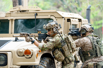 Wide shot of two militaries or soldiers stay in front of humvee car area of car hood and point gun to left side during outdoor practice.