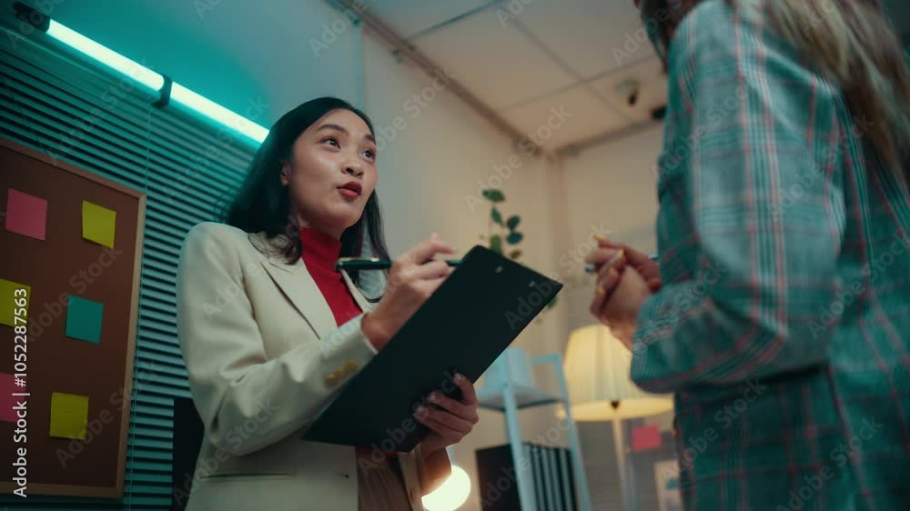 Poster businesswoman holding a clipboard and pen engages in conversation with a colleague in a modern offic
