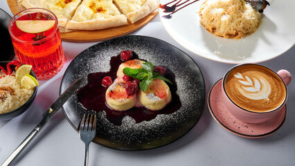 Cheesecakes with jam on a black plate with a cup of coffee. In the background there are many other dishes