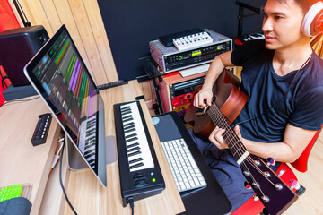asian male musician, producer playing acoustic guitar for recording in home studio