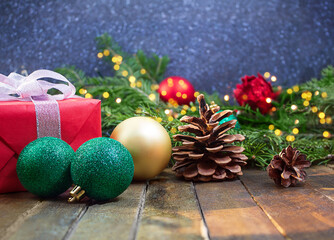 Red gift box with bow, glitter balls, pinecones on wooden background, blurred lights on back. Christmas, New Year, holiday. Copy space