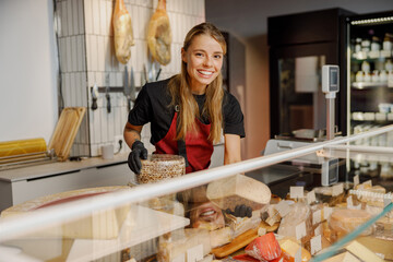 A beaming, smiling employee takes pride as they showcase a diverse array of delicious cheeses in a...