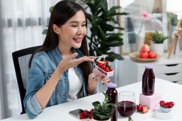 Smiling young beautiful Asian reviewing tasty mixed strawberry and cherry juice detox drinks,...