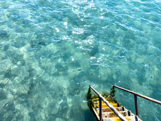 Yellow wooden steps with metal handrails descend into clear turquoise water. Top view creating an...