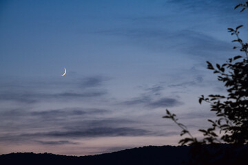Obraz premium Crescent moonrise at dusk over mountains