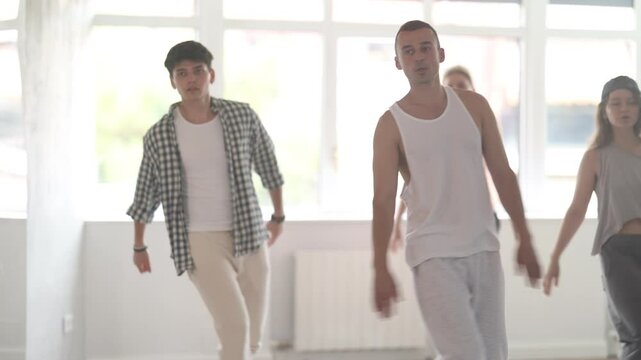 Young man standing performs basic hip hop movements in front of group of students. Developing precise movements, rehearsing arc elements, nae nae moving 