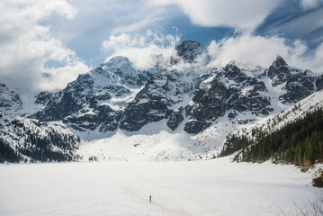Fototapeta premium tranquil view of Morskie Oko in Tatra National Park, Poland, showcasing majestic snow-covered mountains, serene frozen lake, and reflections on a chilly winter day. Winter landscape