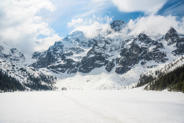 tranquil view of Morskie Oko in Tatra National Park, Poland, showcasing majestic snow-covered mountains, serene frozen lake, and reflections on a chilly winter day. Winter landscape