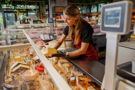 In a busy deli, an employee skillfully slices various cheeses, showcasing the finest artisanal products