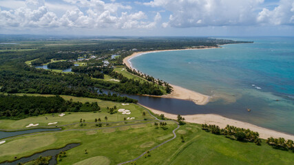 Western Aerial view of Bahia Beach golf resort in Puerto Rico, showcasing green fairways, palm-lined paths, scenic vistas, and ocean views in the distance, all under a clear, blue sky.