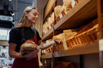 A dedicated young woman meticulously organizes fresh bread in a cozy bakery, highlighting her...
