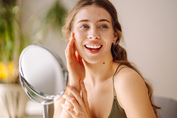 Beautiful woman looking in the mirror, touching her face with her hand.  Pimples, acne, pores,...