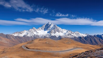 A breathtaking landscape showcases a majestic snow-covered peak against a vibrant blue sky, with a curving road tracing through the arid terrain below, offering a serene escape into nature