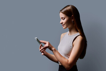 Young beautiful woman using smartphone on gray background, profile view, copy space