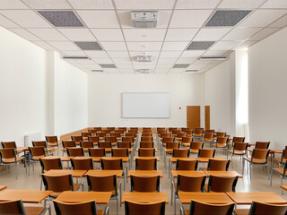 Empty classroom with rows of wooden desks and chairs, bright lighting, and a large whiteboard on the wall during the daytime