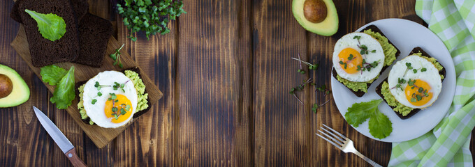 Avocado toasts for breakfast with rye bread, avocado puree, fried egg and microgreen on the wooden background. Top view. Copy space.