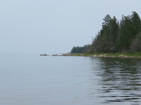 Waters of Lake Superior in Small Bay of Drummond Island with Tree Covered Forest Land Jutting Out under Misty Sky
