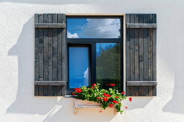 A charming wooden window surrounded by vibrant flowers on a sunny day in a quaint rural setting