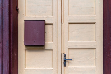 A rustic yellow door features a mailbox, framed by wooden siding on a sunny day.