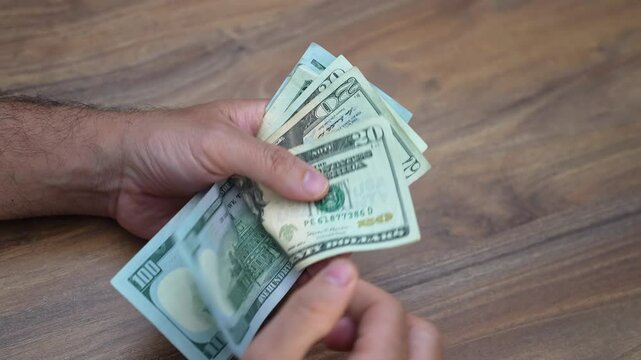 Male worker carefully counts dollar banknotes from various jobs evaluating earnings and budgeting for rent and essentials showing hustle required to make ends meet