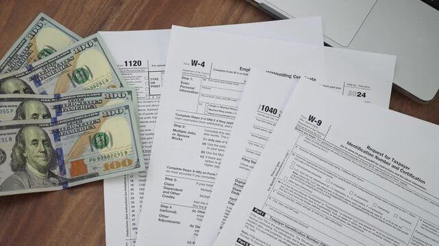 Hundred-dollar bills placed near several tax forms including Request for Taxpayer Identification Number and Certification on top on wooden table in office