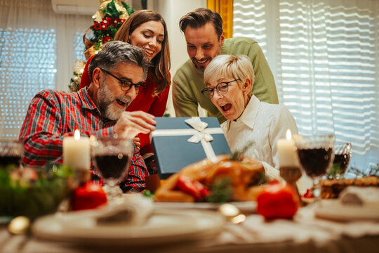 Family having christmas dinner together opening present - Powered by Adobe