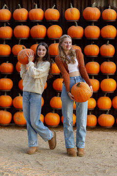 two teenage girls proudly holding their pumpkin in front of pumpkin wall