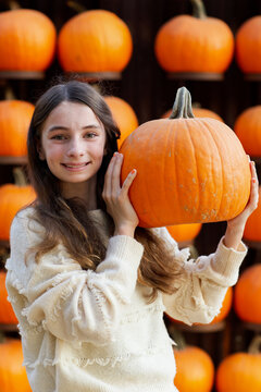 portrait of a brown haired girl with green eyes proudly showing a large pumpkin