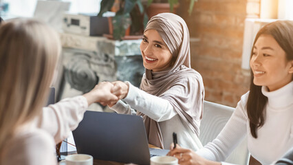Obraz premium Two multiracial girls business colleagues shaking hands during group meeting in office, close up