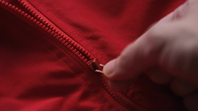 A man unzipping his red jacket. Close up.