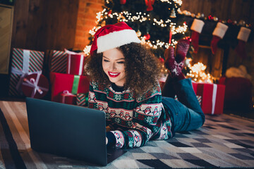 Full size photo of pretty young woman lying floor use laptop christmas festive illumination apartment indoors