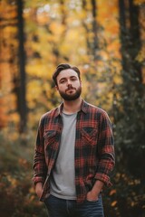 A contemplative man in a flannel shirt stands among trees with vibrant autumn leaves, capturing reflection and seasonality.
