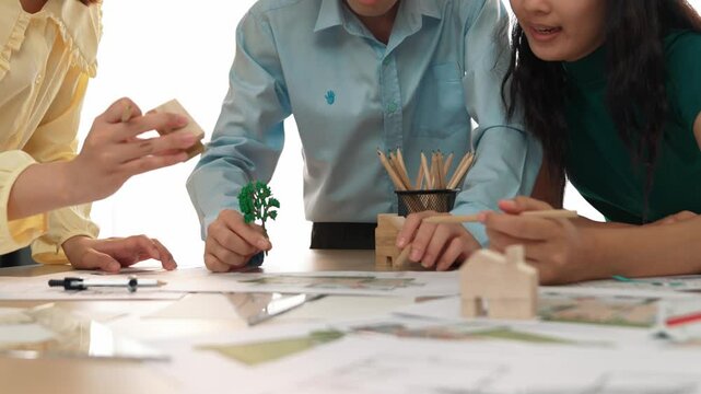 Architect and safety engineer discuss about position of tree use blueprint, model on table with architectural document, measurement tool and wooden block scatter around at modern office. Delineation.