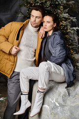 A couple in warm winter jackets shares a tender moment near snow-covered pine trees, embracing the holiday spirit.