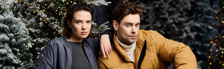A couple in cozy winter jackets enjoys a magical snowy landscape filled with pine trees and festive cheer.