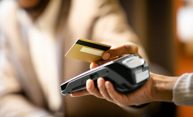 Unrecognizable afro businessman in suit giving credit card to barman paying with gold credit card in cafe, close up