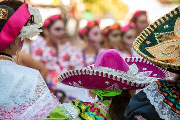 Folklorico Dancers with colorful hats watch a performance during a Día De Los Muertos festival.
