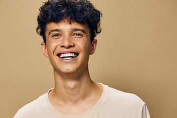 Happy young man smiling with curly hair against a plain beige background, exuding joy and...