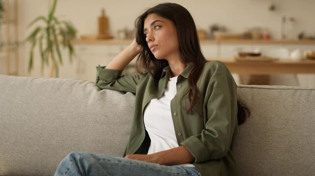 Boring sad upset frustrated stressed Arabian woman Indian girl female Hispanic lady exhausted sorrowful disappointed holding mobile phone smartphone unwanted pregnancy problem thinking at home couch