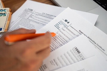 Fototapeta premium Person filling out a W-4 tax form with an orange pen, euros and a laptop on the side. Tax preparation and financial documentation process 