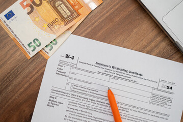 Obraz premium Close-up of W-4 tax form with orange pen and euro banknotes on wooden desk. Tax preparation and financial management concept 