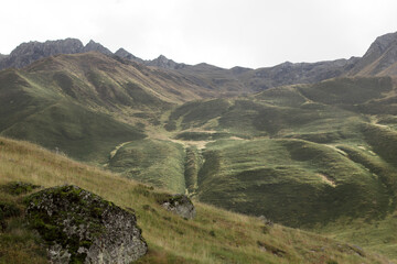 A vast green hillside with gentle slopes leading up to rugged mountain peaks, covered with a patchwork of grass and moss in Georgia