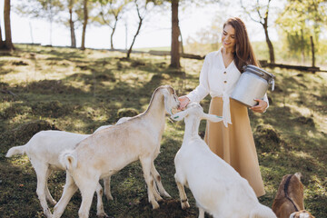 Woman Feeding Goats on a Sunny Pasture, Embracing Rural Life and Nature with a Joyful Expression