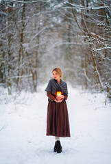 Naklejka premium Portrait of beautiful blonde girl in medieval dress and woolen scarf in winter snowy forest. Young worker in rural scene with flashlight.Colorful fairytale art work.