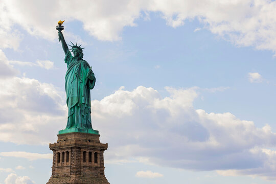 Iconic Statue of Liberty against a partly cloudy sky, symbolizing freedom and welcoming visitors to New York City.