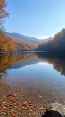 Fototapeta premium Serene Autumn Reflection: A tranquil lake in the embrace of vibrant autumn foliage, its crystal-clear waters mirroring the majestic mountains and colorful trees.