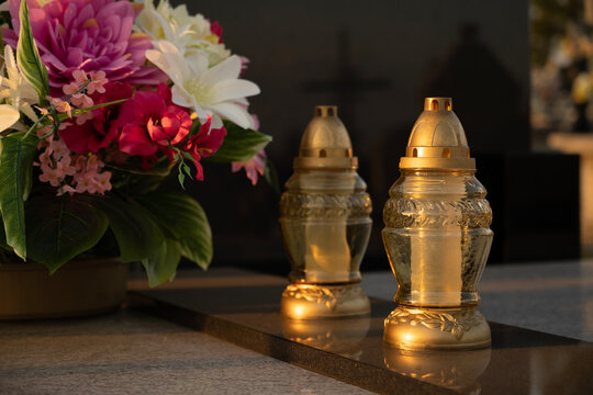 A tomb decorated with candles and flowers with cementary in the background.