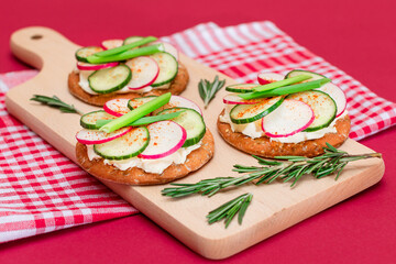 Light Breakfast or Diet Eating - Crispy Cracker Sandwich with Cream Cheese, Fresh Cucumber, Green Onions and Radish on Wooden Cooking Board on Magenta Background