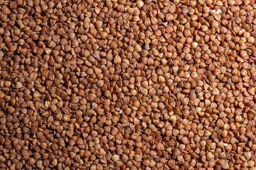 Fototapeta premium Dry Uncooked Brown Buckwheat Groats Background - Top View, Flat Lay. Raw Large Buckwheat Grains. Russian, Ukrainian and Belarusian Culture